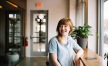 smiling woman sits at a bright window